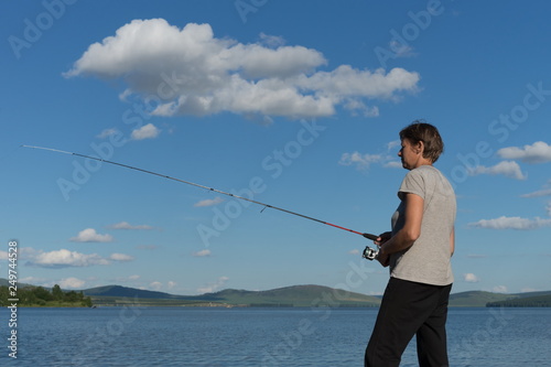Woman fisherman catches a fish from a blue lake against a blue sky with clouds. Natural shot.