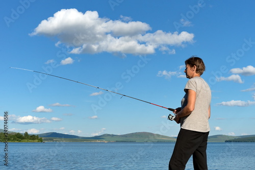 Woman fisherman catches a fish from a blue lake against a blue sky with clouds. Bright shot.
