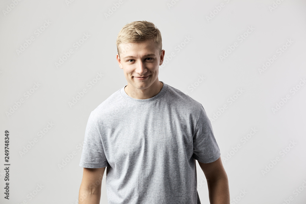 Fototapeta premium Smiling blond guy dressed in a white t-shirt stands on the white background in the studio