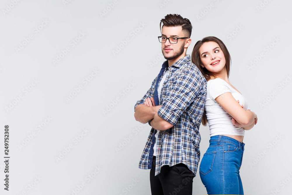 Concept of multiethnic cooperation and friendship. Attractive woman in denim clothes and causasian smiling man in jeans shirt are standing back to back against background. Concept of multiethnic cooperation and friendship. Attractive woman in denim clothes and causasian smiling man in jeans shirt are standing back to back against background.
