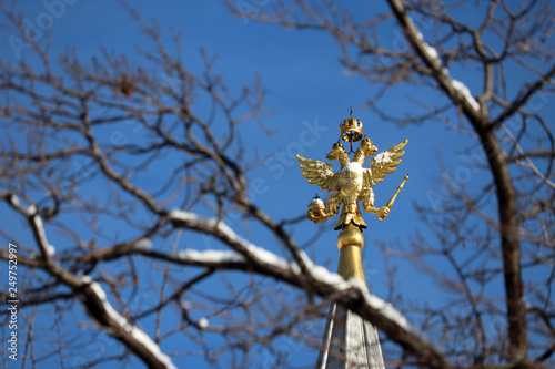 Snow covered double-headed eagle, symbol of Russia isolated on blue sky background. Golden russian emblem on the top of tower on Red square in Moscow, view through tree branches, winter weather