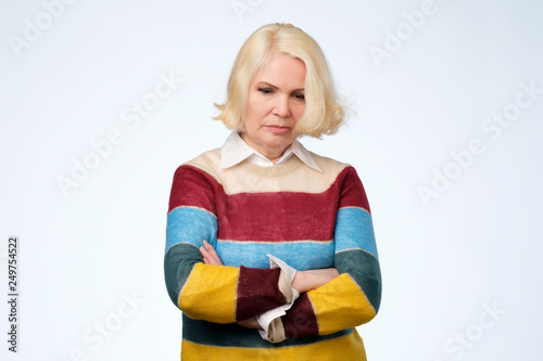 senior woman holds hands crossed over chest, looks with sad expression.
