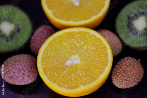 still life of citrus, juicy kiwi and orange in the cut and Litchi chinensis on a dark background
