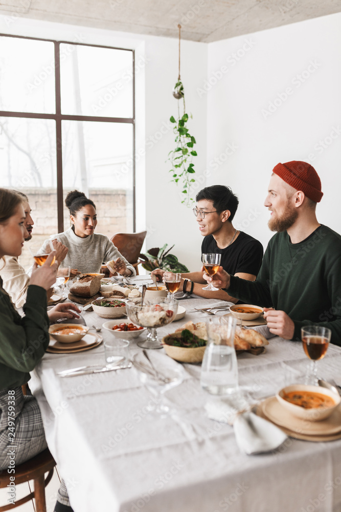 Group of cool international friends sitting at the table full of food thoughtfuly talking together. Young colleagues having lunch spending time in cafe
