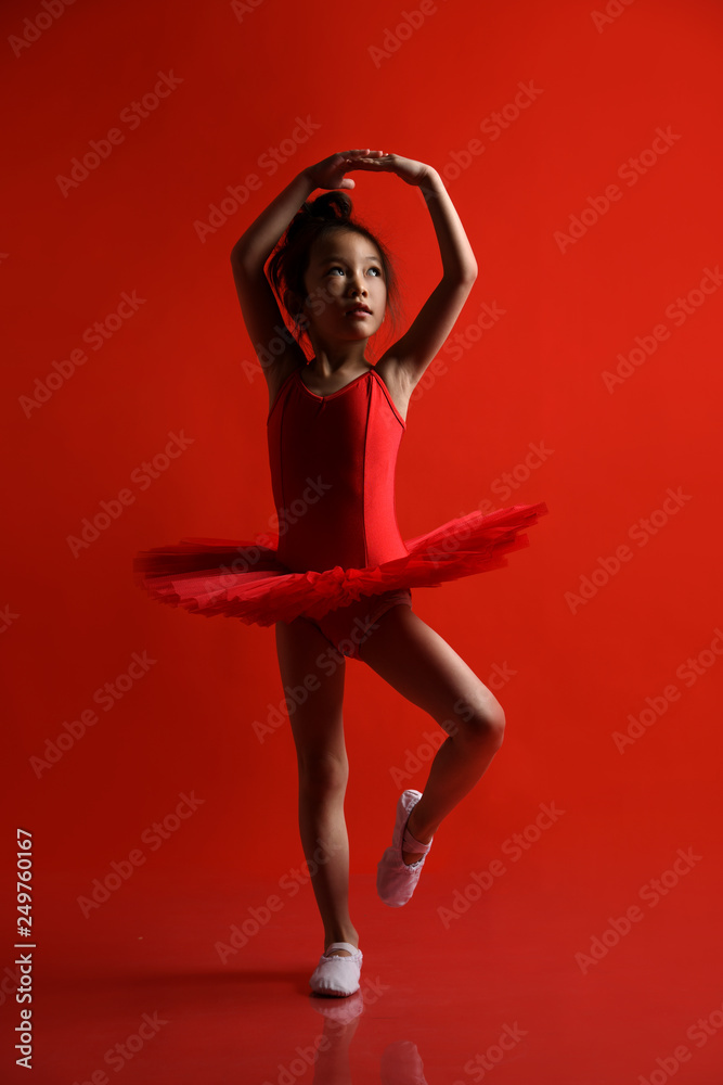 Cute little girl ballerina dancer in beautiful dress is dancing jumping on red background Cute little girl ballerina dancer in beautiful dress is dancing jumping on red background