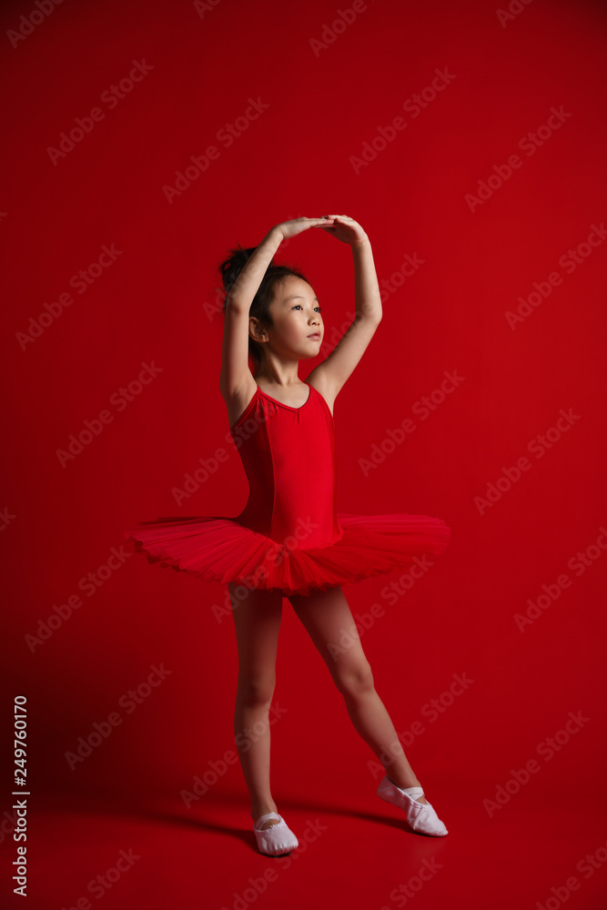 Cute little girl ballerina dancer in beautiful dress is dancing jumping on red background 