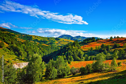 Beautiful countryside landscape with forested hills and haystacks on a grassy rural field in mountains