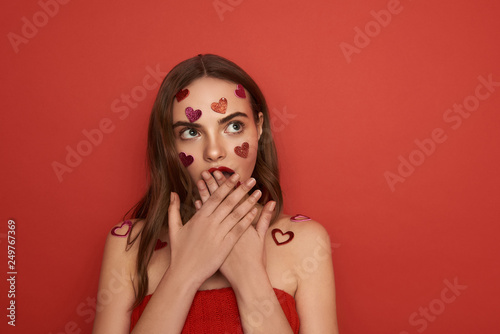 Scared young lady closing her mouth with arms on red background