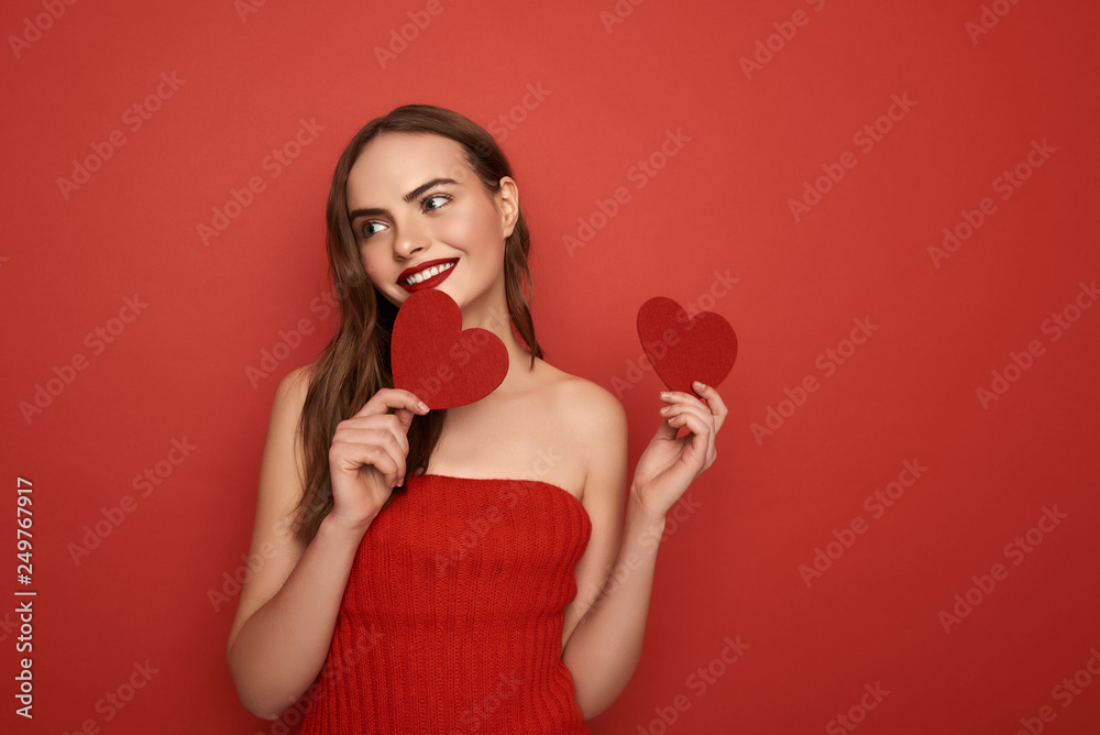 Glamorous model keeping decorative hearts in arms on red background Glamorous model keeping decorative hearts in arms on red background