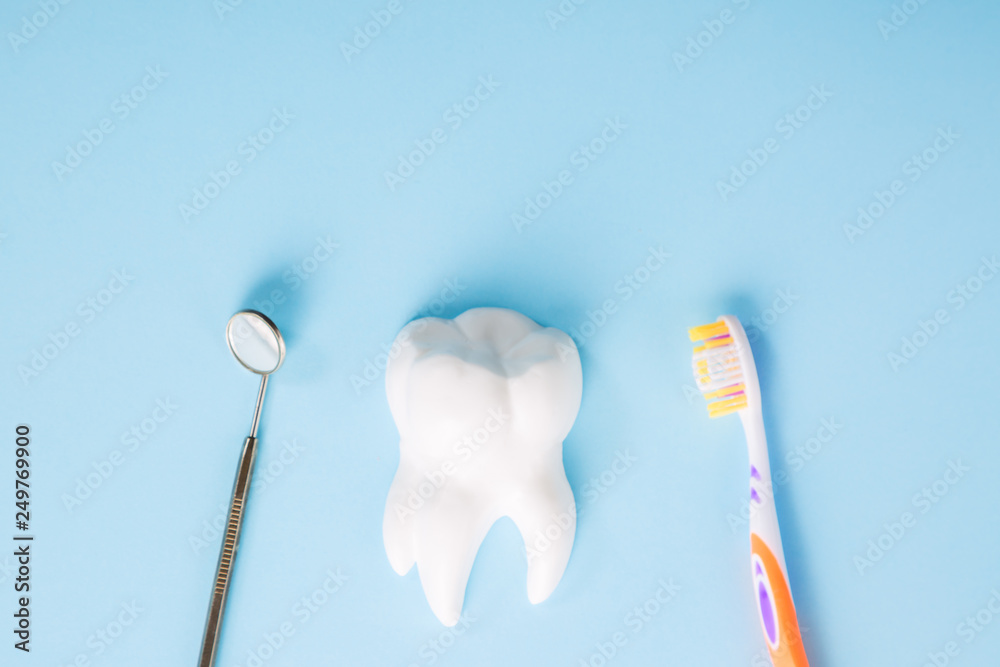 Professional dental mirror near white tooth model and toothbrush on light blue background with free space. Dental health and teethcare concept. Professional dental mirror near white tooth model and toothbrush on light blue background with free space. Dental health and teethcare concept.