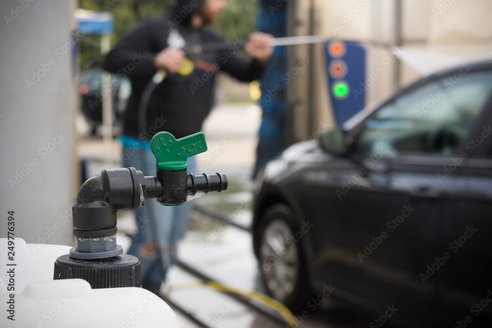 Close Up of a Bottle Full of Soap on Blurred Background of a Man Using Water Pressure Machine to Wash a Car