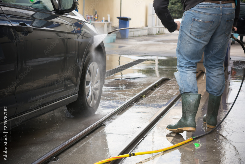 Man Using Water Pressure Machine to Wash a Car on Blurred Background