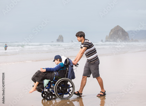 Young man pushing disabled brother in wheelchair on beach