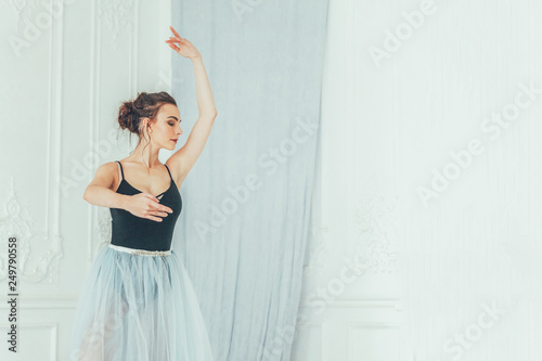 Young classical ballet dancer woman in dance class. Beautiful graceful ballerina practice ballet positions in blue tutu skirt near large mirror in white light hall