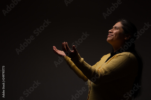 Fototapet Hispanic Christian Woman Praying with Open Arms on Dark Grey Background 