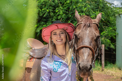 Beautiful blonde cowgirl with hat standing near the horse ranch background © Brastock Images