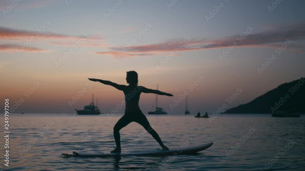 Young woman doing yoga on sup board with paddle at sunset. Concept of harmony with the nature, free and healthy living, freelance, remote business.