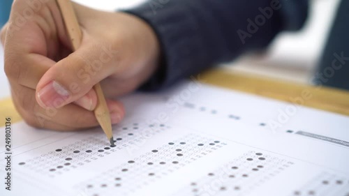 School / university Students hands taking exams, writing examination room with holding pencil on optical form answers paper sheet on desk doing final test in classroom. Education assessment Concept