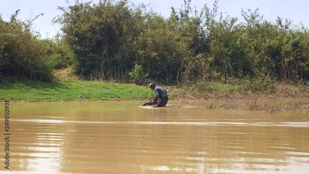 fisher - waist-deep in water - is shaking and removing sand, from the push basket fisher - waist-deep in water - is shaking and removing sand, from the push basket