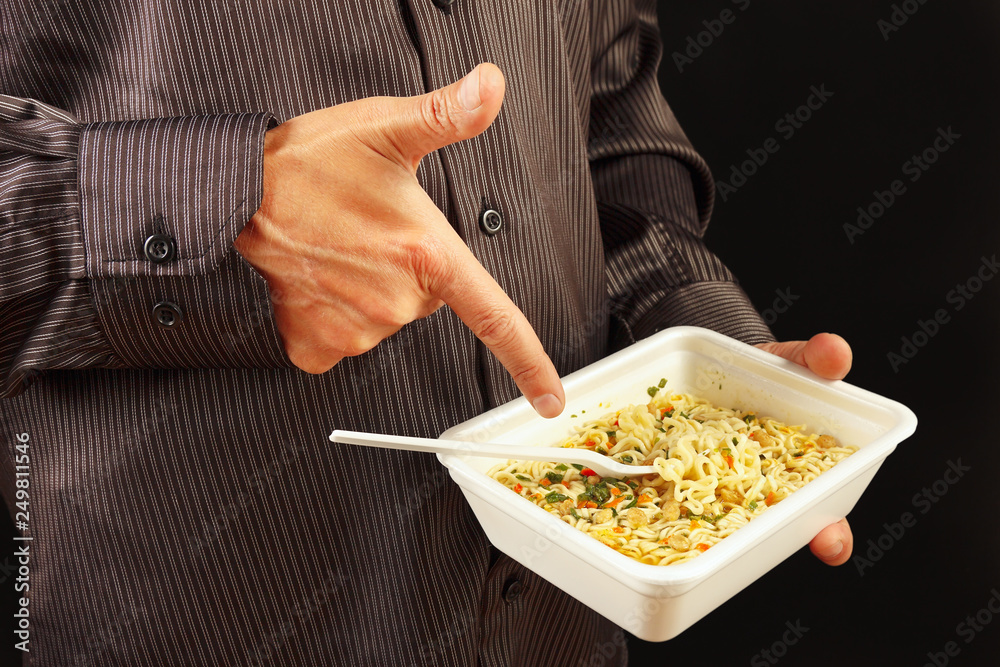 Man in black shirt recommends instant noodles on a black background close up Man in black shirt recommends instant noodles on a black background close up