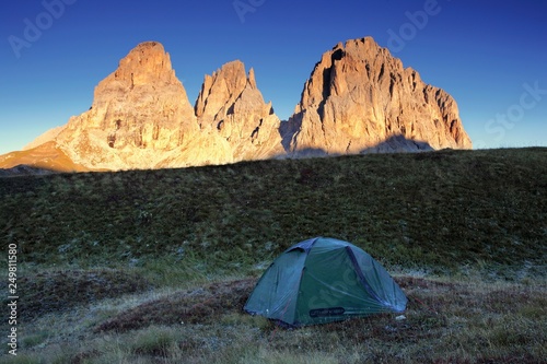 Summer camping  night  shining green tent on pasture. Night shot  long exposure. Alps Mountains landscape panoramic view. Gorgeous autumn day in Dolomites  Italy. Sassolungo mountain range. Sella pass