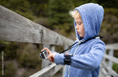 Young boy on a wooden bridge of a national park taking pictures with a action camera