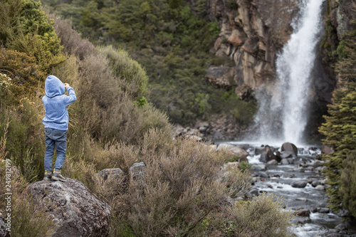 Young boy in a national park admiring and taking photos of a waterfall