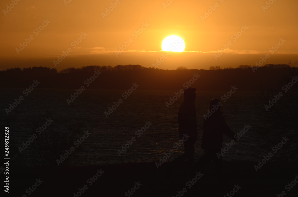 Sunset over the sea, people seen as black silhouettes towards the sea.