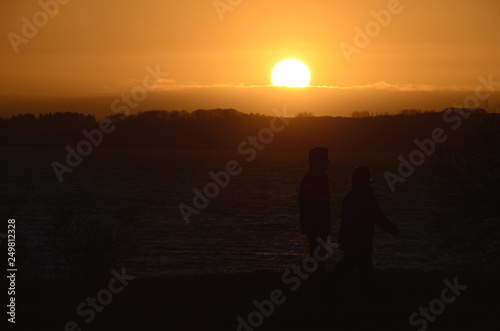 Sunset over the sea, people seen as black silhouettes towards the sea. © Kim