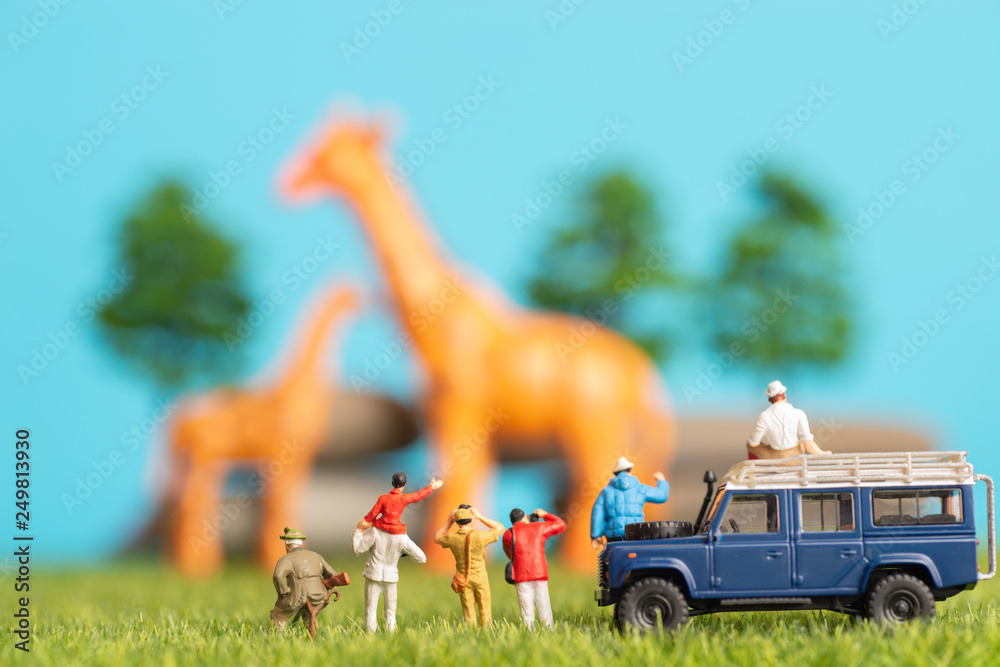 Miniature toys of a group of people on safari trip watching giraffes