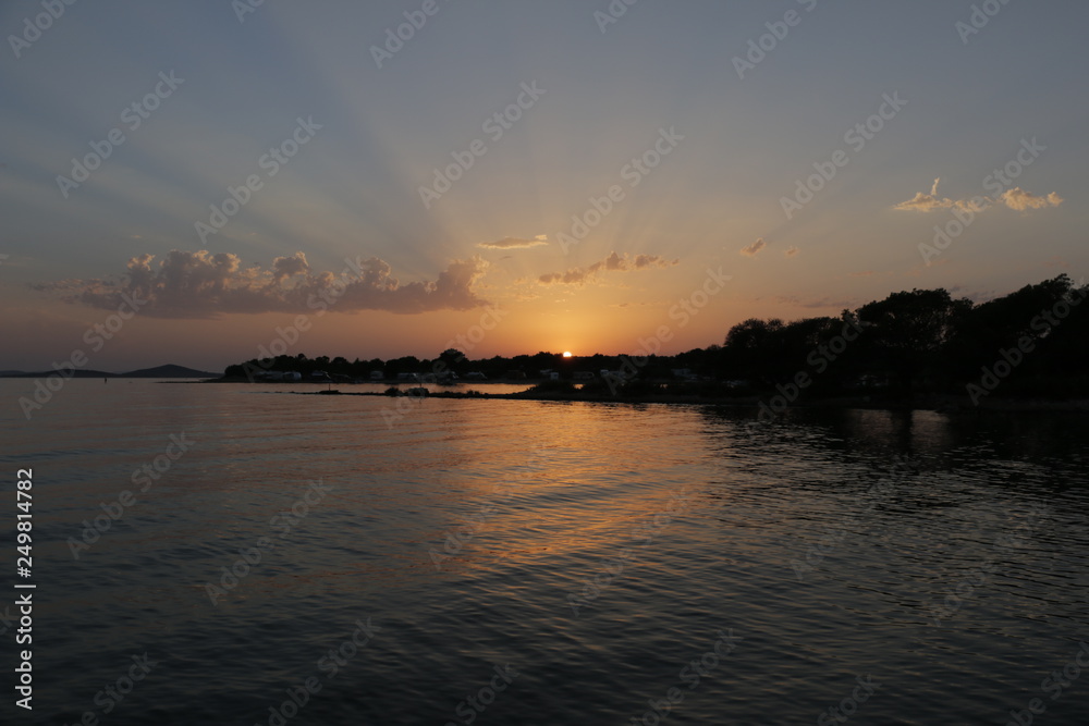 Sunset on the seashore. Summer, warm, holiday, evening. Twilight on the Adriatic Sea in Croatia. Colorful, orange, blue sky. Beautiful dusk. Pleasant, calm end of the day.  Beautiful sun beams.