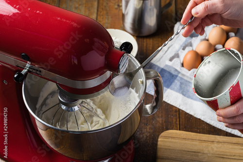 pouring sugar into bowl of red standing kitchen aid mixer on wooden table