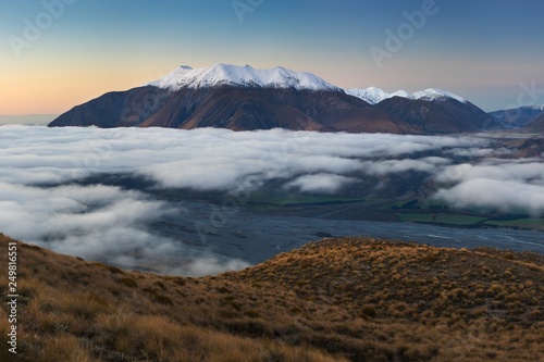 The valley is flooded in mist in a mountain environment. Over the fogs, only the high peaks of the mountains rise beneath the sunny sky. Misty morning on the Southern Island New Zealand, Christchurch 