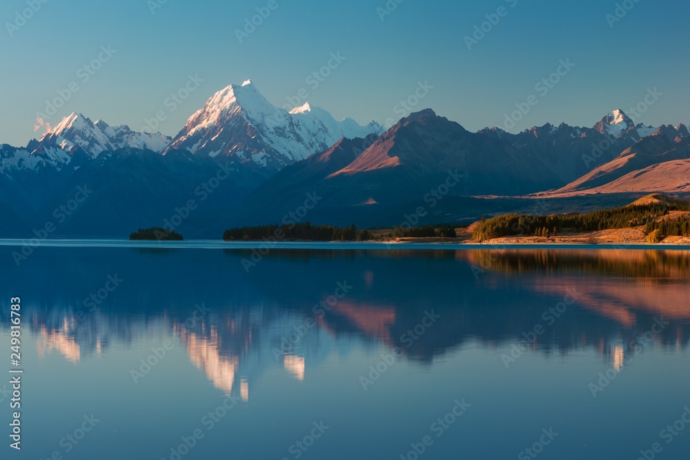 Snowy mountain range reflected in the still water of Lake Pukaki, Mount Cook, South Island, New Zealand. The turquoise water comes from Mt. Cook and Tasman glacier. Popular travel destination