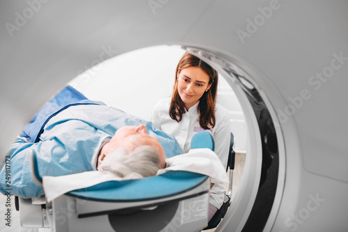 Radiographer reassuring senior man going into CT scanner in hospital