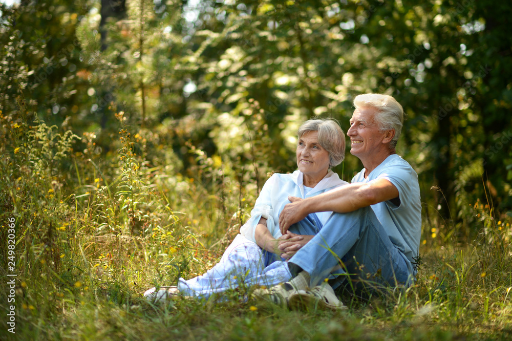 Portrait of nice mature couple sitting on green grass in summer park