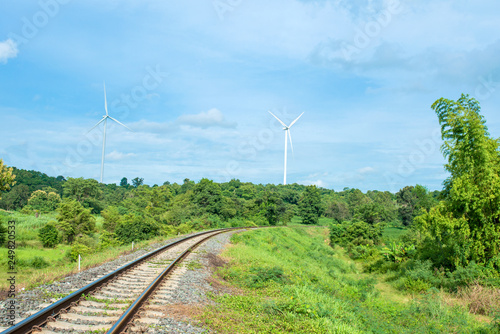 Railroad tracks stretches. green trees and wind turbines with the blue sky as the background. An idea of using energy in traveling Or to save energy on the trip. feel fresh and relax to traveling