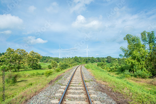 Railroad tracks stretches. green trees and wind turbines with the blue sky as the background. An idea of using energy in traveling Or to save energy on the trip. feel fresh and relax to traveling