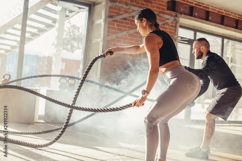 Caucasian fit attractive couple in sports clothing concentrated on the exercise with battle rope requiring increased effort and strength, standing at well lit fitness centre with loft brick interior photo