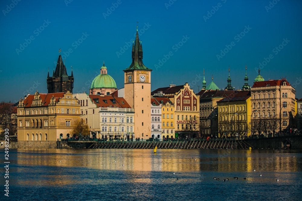 Prague, Czech Republic / Europe - February 16 2019: View of Novotneho footbridge and historical buildings, reflection in Moldau river, bright sunny cold day, blue sky, seagulls and ducks on water