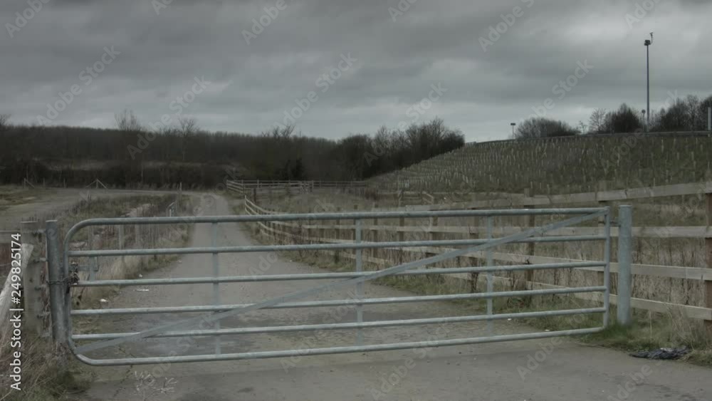 Dirt track with metal gate under a grey winter sky. CCTV surveillance camera to right of frame. Dirt track with metal gate under a grey winter sky. CCTV surveillance camera to right of frame.