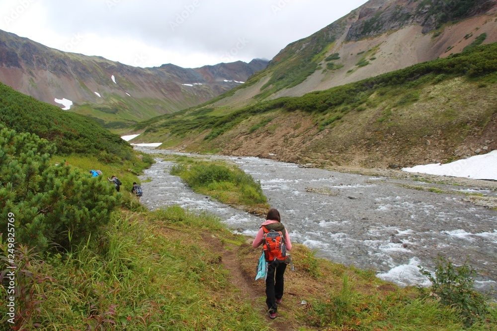 Tourists walks by mountain Tahkoloch river in the caldera of the extinct Vachkazhets volcano on the Kamchatka Peninsula, Russia.