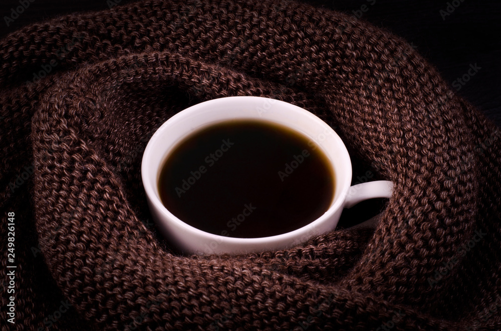 Obraz premium Black coffee in a white cup with a brown scarf. Winter comfort