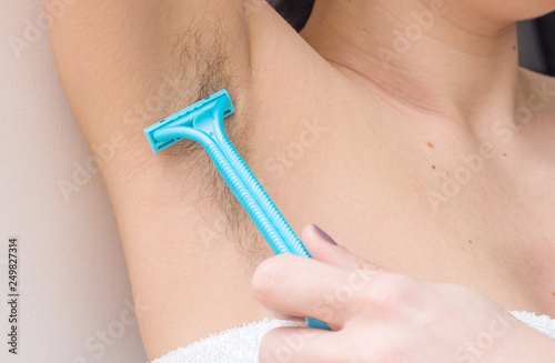 Female unshaved armpits or woman with long hair underarm, depilation, hair removal concept. Young woman shaves hairy armpits with a disposable razor.  Close-up, selective focus.