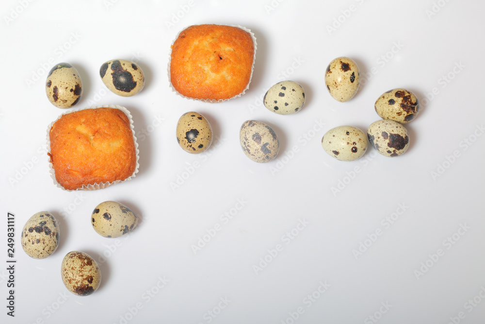 Obraz premium Quail eggs lie on the white surface. Nearby are cupcakes. Next to the box with a gift wrapped in wrapping paper and tied with a ribbon.