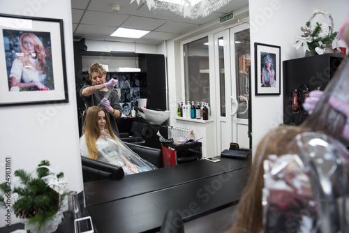 Professional hairdresser putting color mask dyeing hair of woman in beauty salon