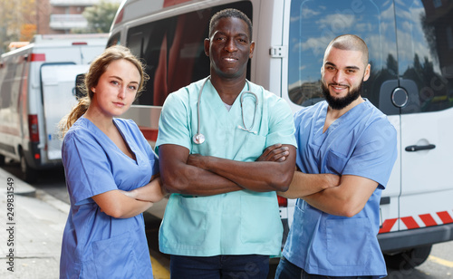 Portrait of three paramedicals in uniform near ambulance car