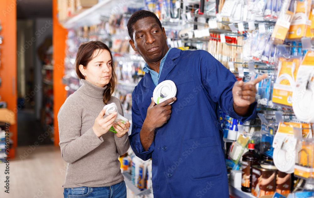 Competent seller consulting young woman about purchase of supplies for household works in store