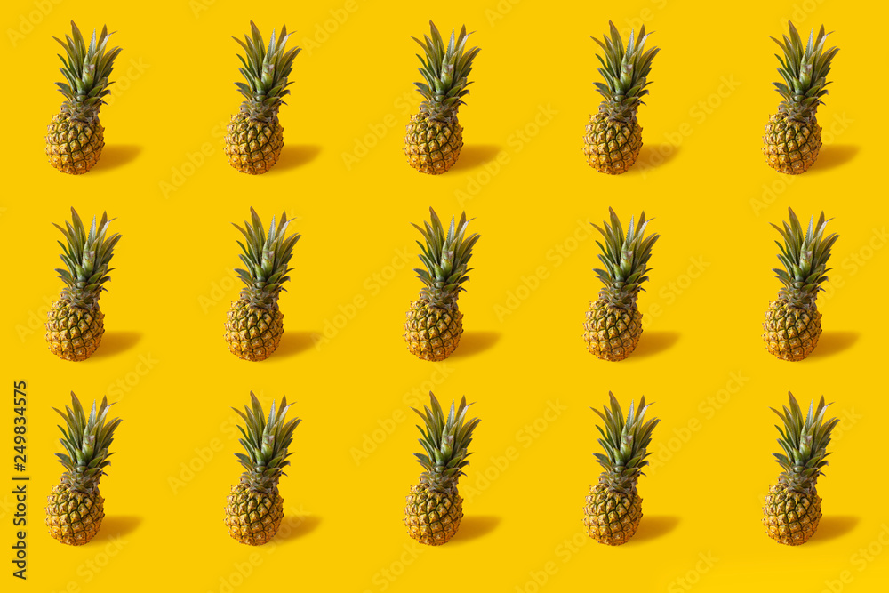 Fototapeta premium Summer colorful fruit minimal pattern of fresh pineapples on yellow background with shadow