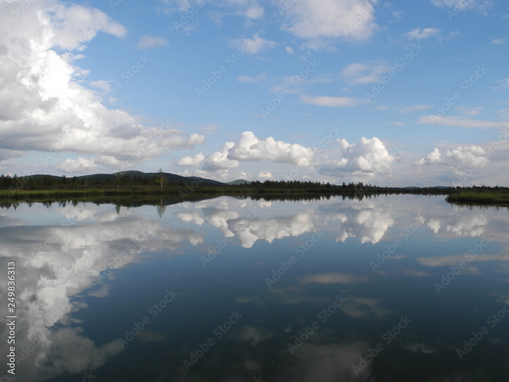 Reflection of blue sky with white clouds in calm still water of a mountain lake